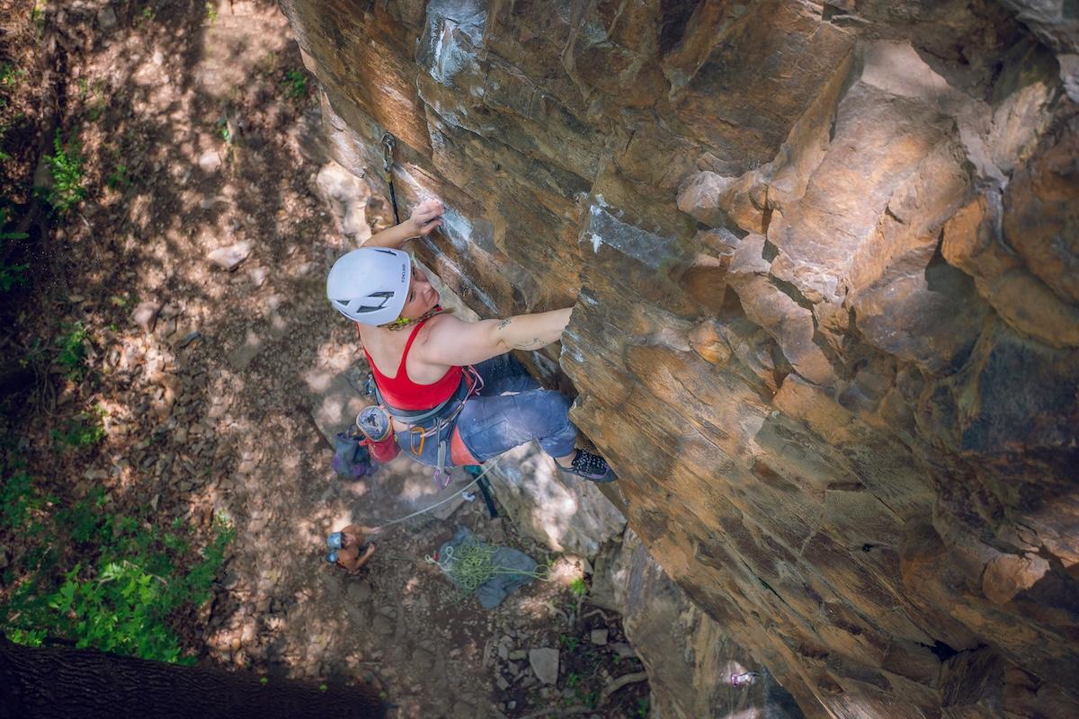 Climber in red top scaling a rocky cliff, wearing a helmet.