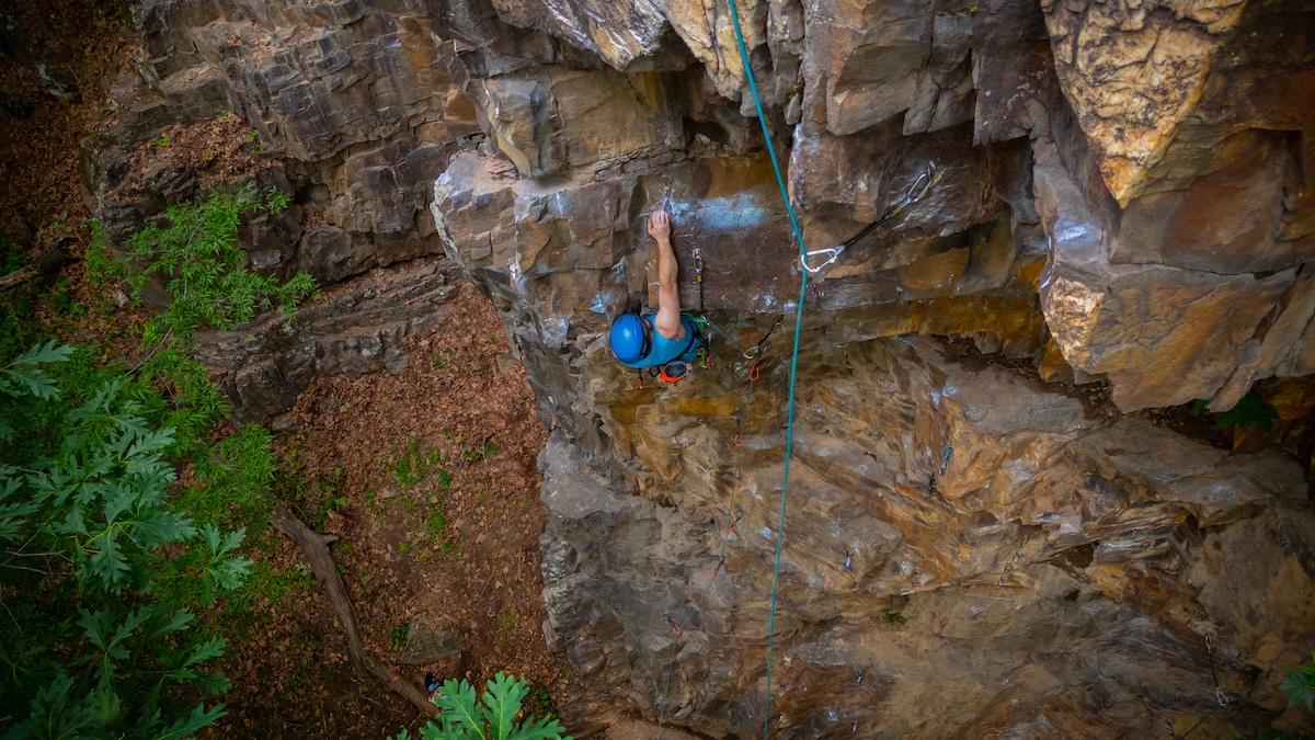 Rock climber ascending a cliff with a blue helmet.