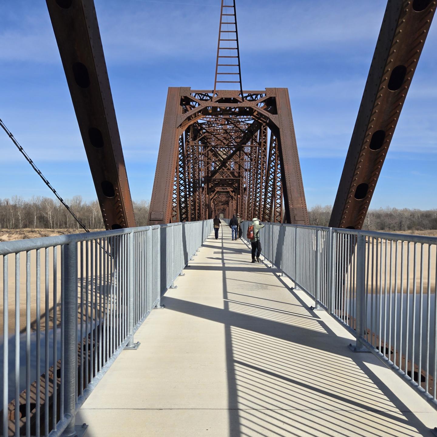 Bridge with metal beams under a blue sky over Arkansas River.