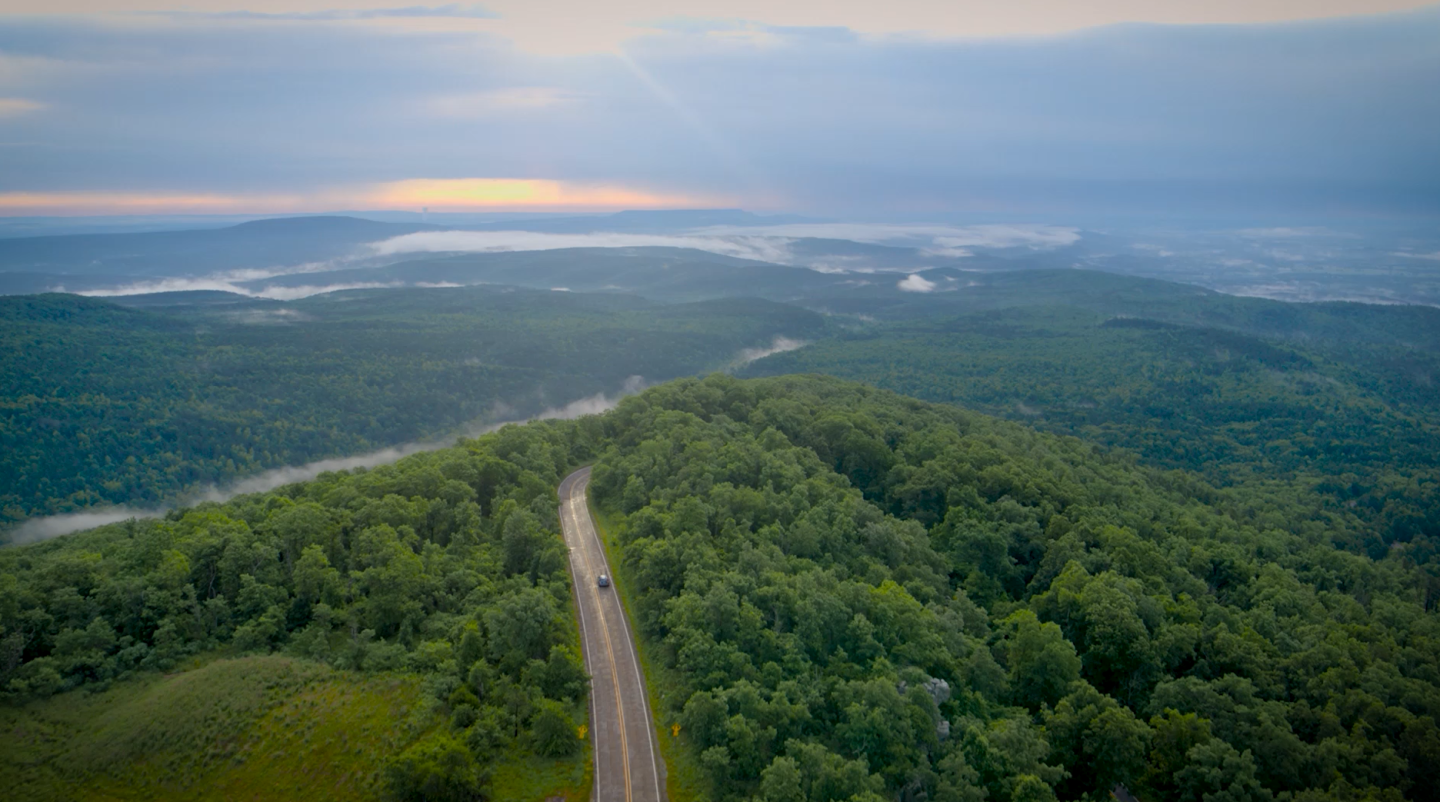 Aerial view of a winding road through lush green hills at sunrise.