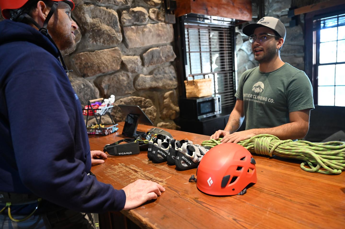 Customer in climbing gear talking to a salesperson at a wooden counter.