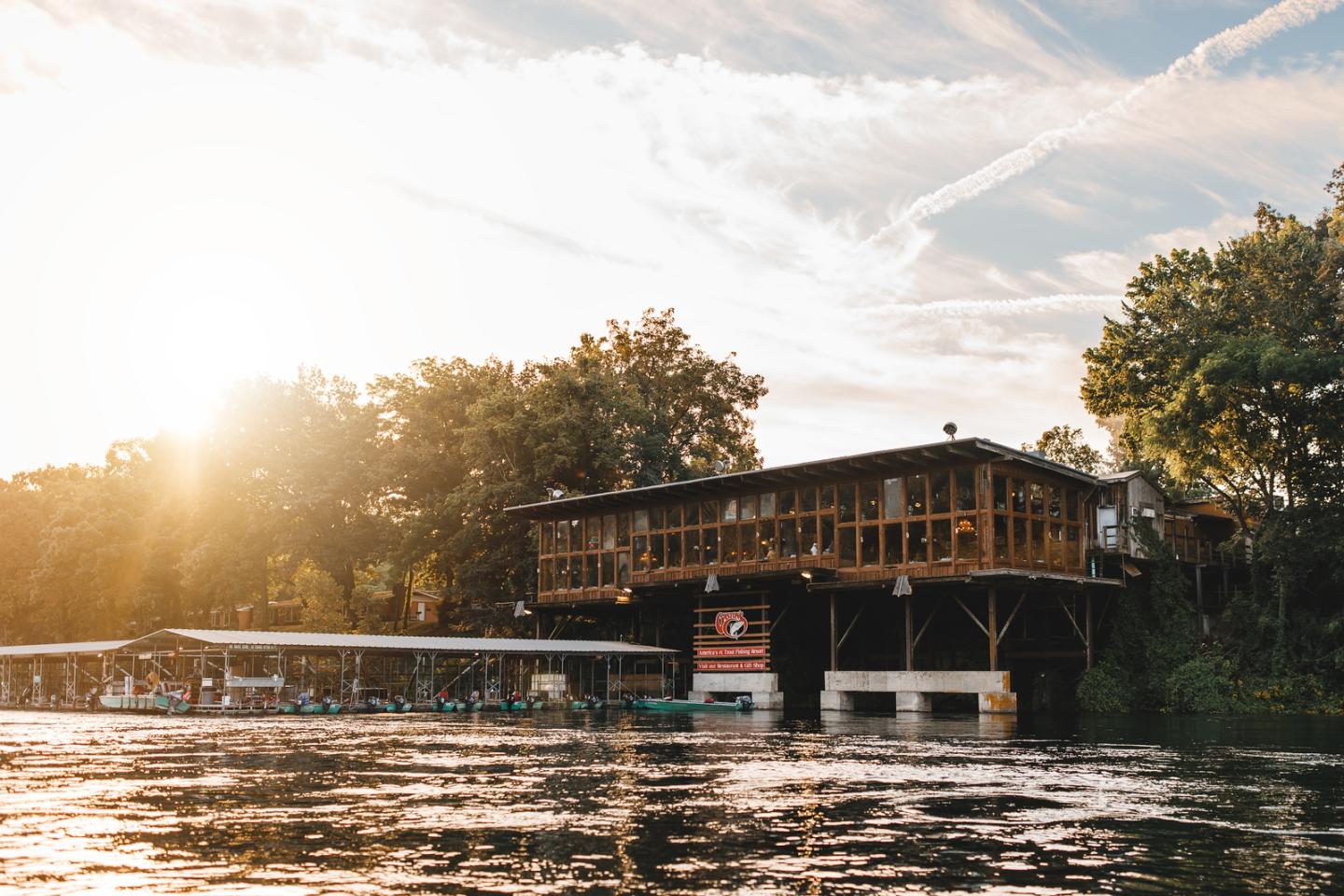 Lakeside house at sunset, surrounded by trees and water.