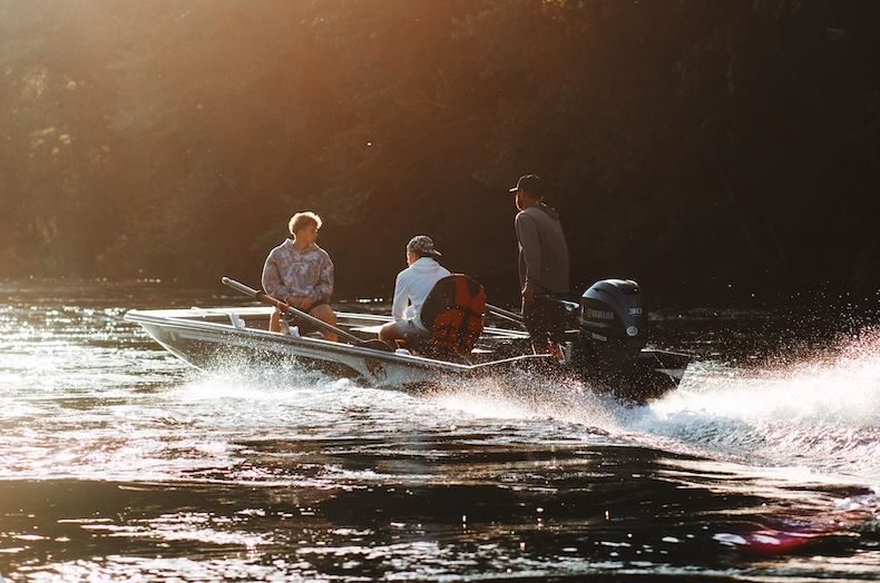Three people on a boat moving through water at sunset.