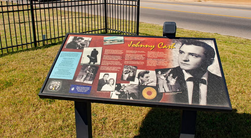 Informational sign about a famous musician, featuring photos and text, displayed on grass.