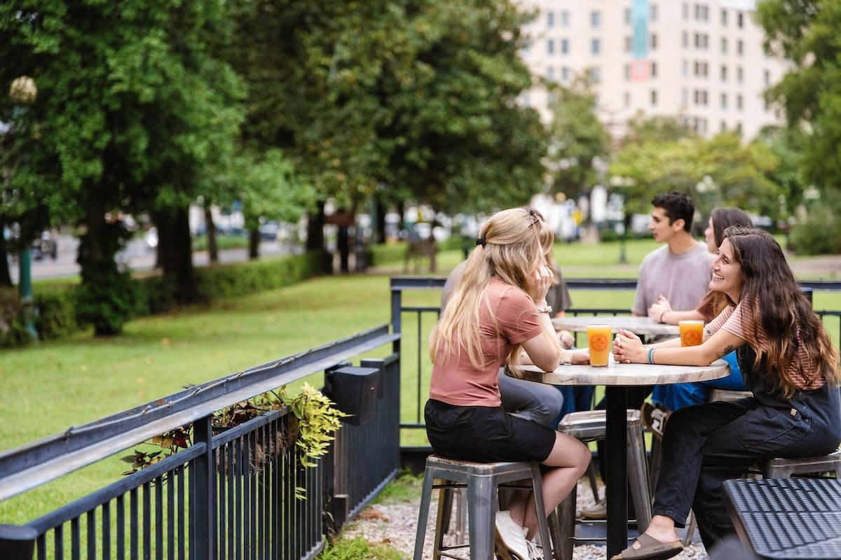 Dining outside, a group of friends shares drinks and conversation on a sunny day.