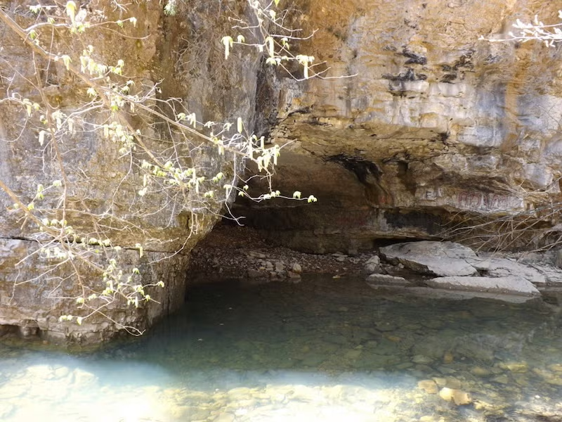 Rocky cave entrance by clear, shallow water.