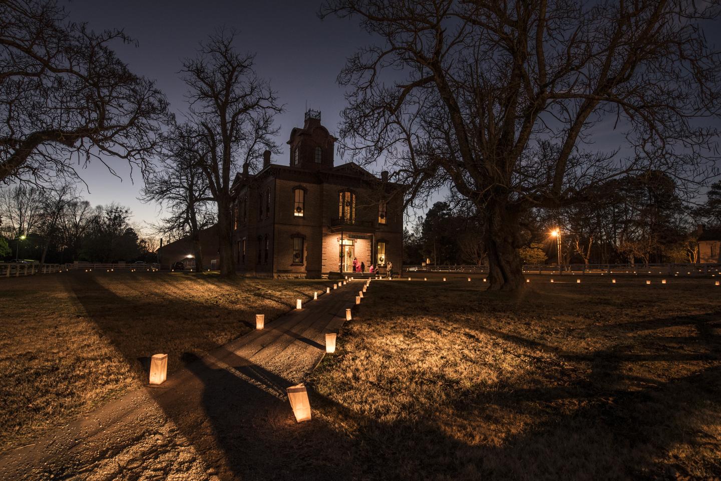 Historic house at dusk, path lit by lanterns.