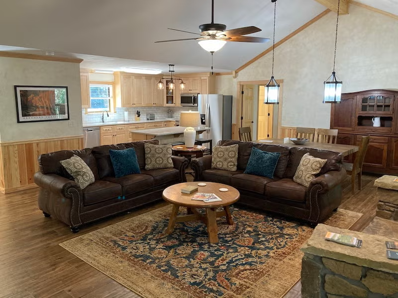 Cozy living room with brown sofas, rug, and kitchen in the background.