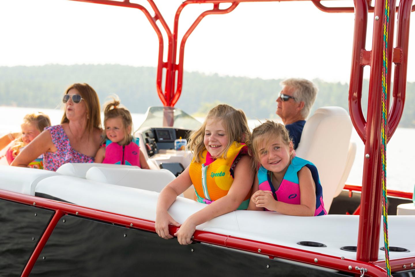 Family enjoys a boat ride on a sunny day, children in colorful life jackets.