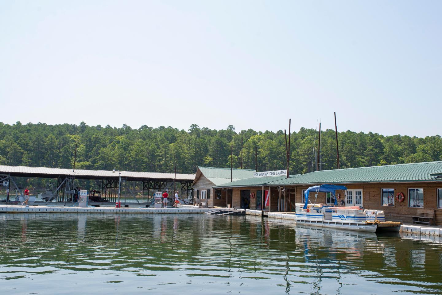 Boathouses on a calm lake with trees in the background.