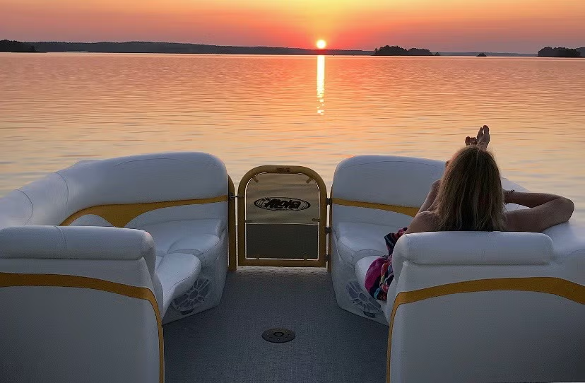Boat on a lake at sunset, person relaxing on rear seat.