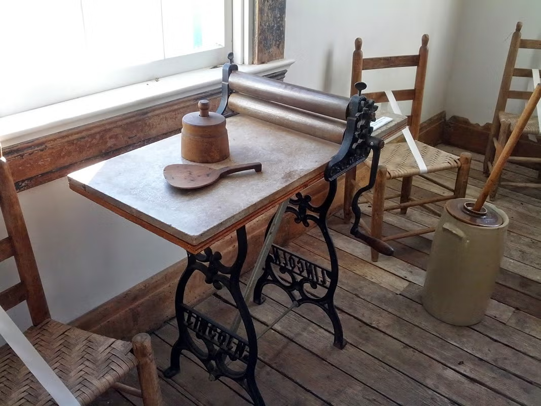 Antique washboard and items on a wooden table, surrounded by chairs.