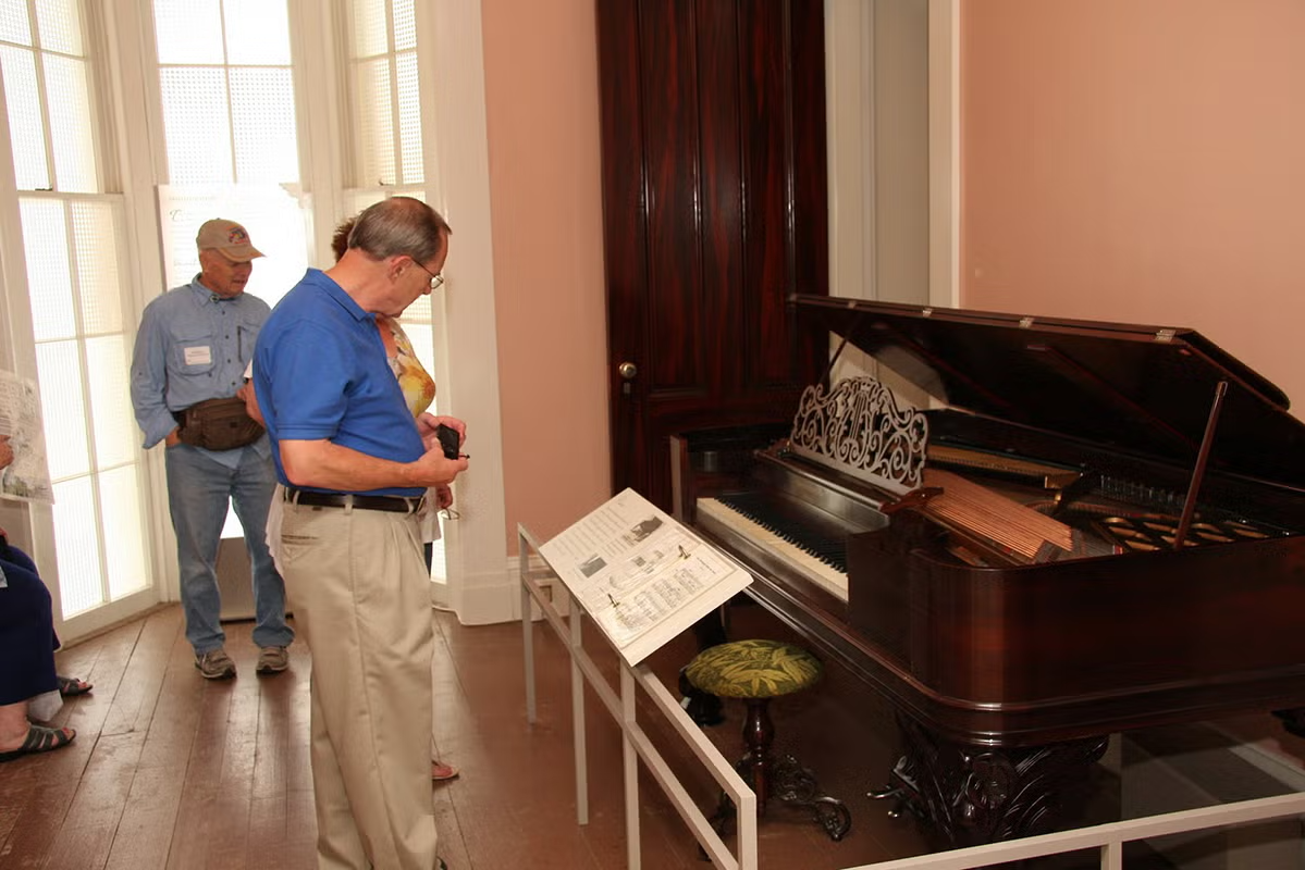 Visitors viewing an antique piano in a museum setting.