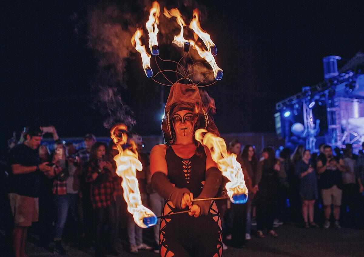 Fire performer juggling torches at night event, surrounded by a crowd.