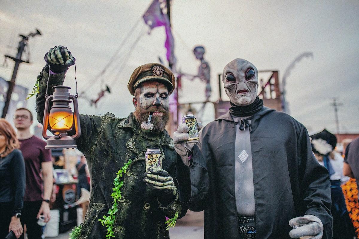 Two people in elaborate costumes, one holding a lantern, at a festive outdoor event.