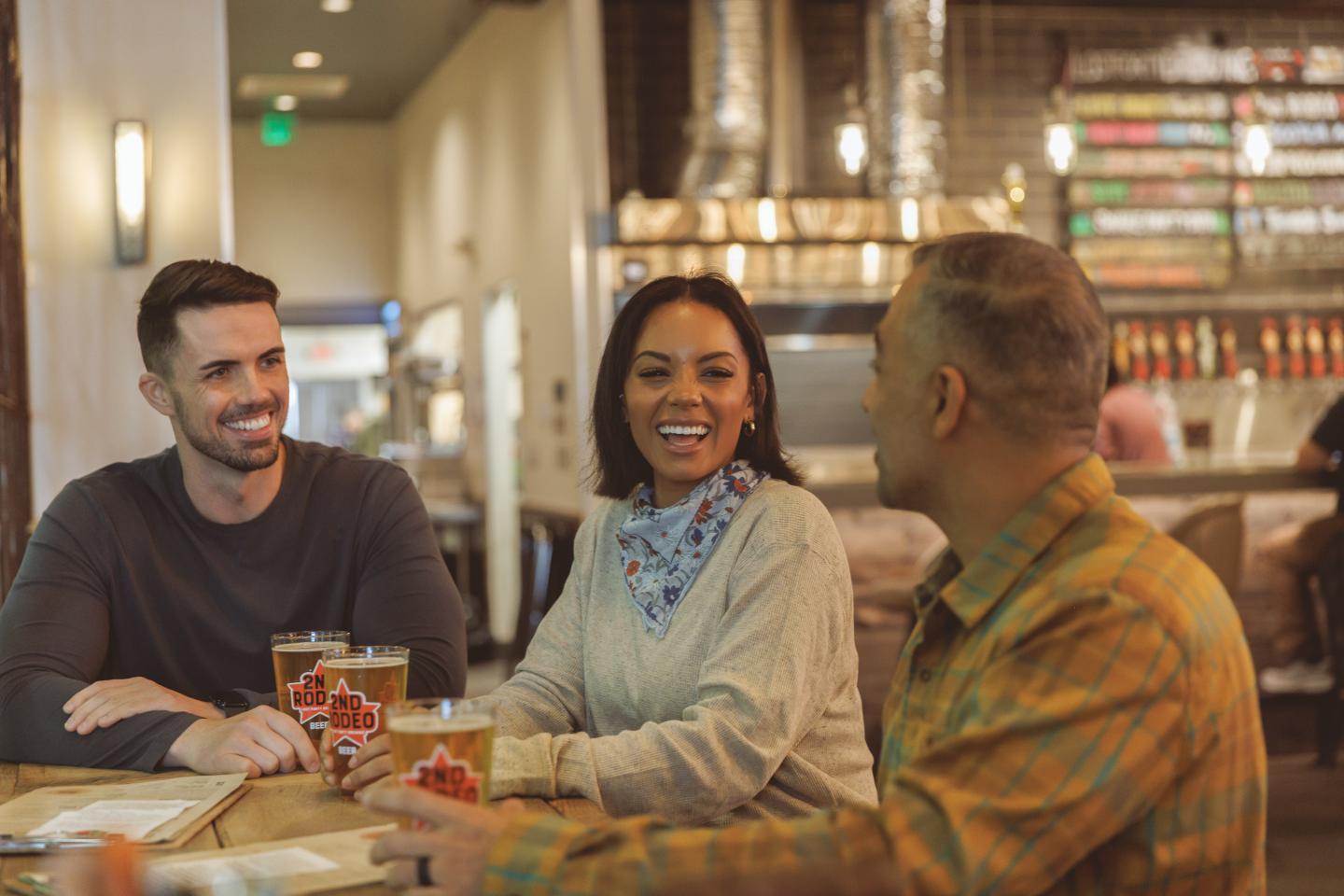 Three people smiling and chatting at a Lost Forty bar table with drinks.