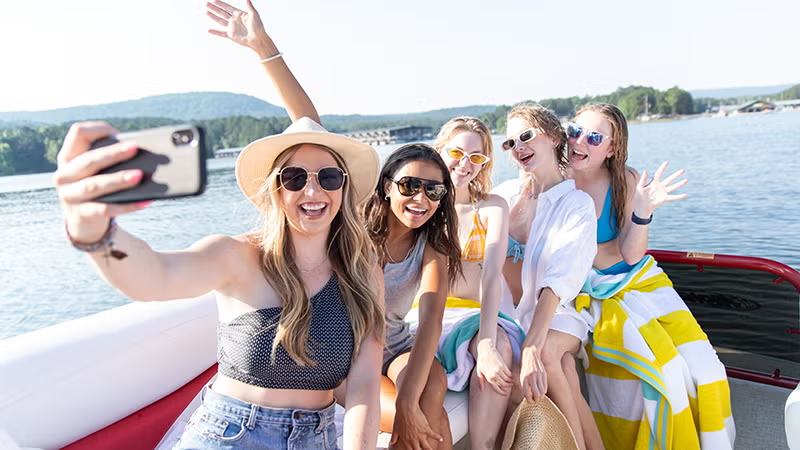 Friends on a boat taking a selfie, smiling and wearing sunglasses.
