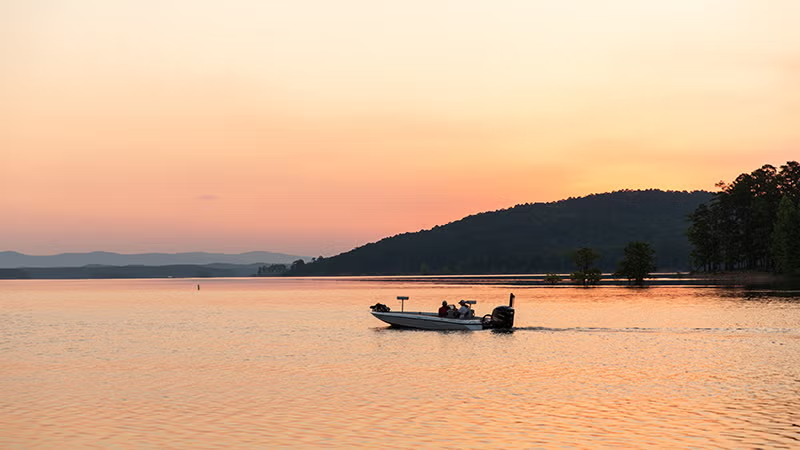 Boat on a lake at sunset with mountains in the background.