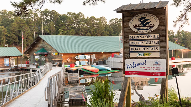 Lake marina with a dock, boats, and a welcome sign in a wooded area.