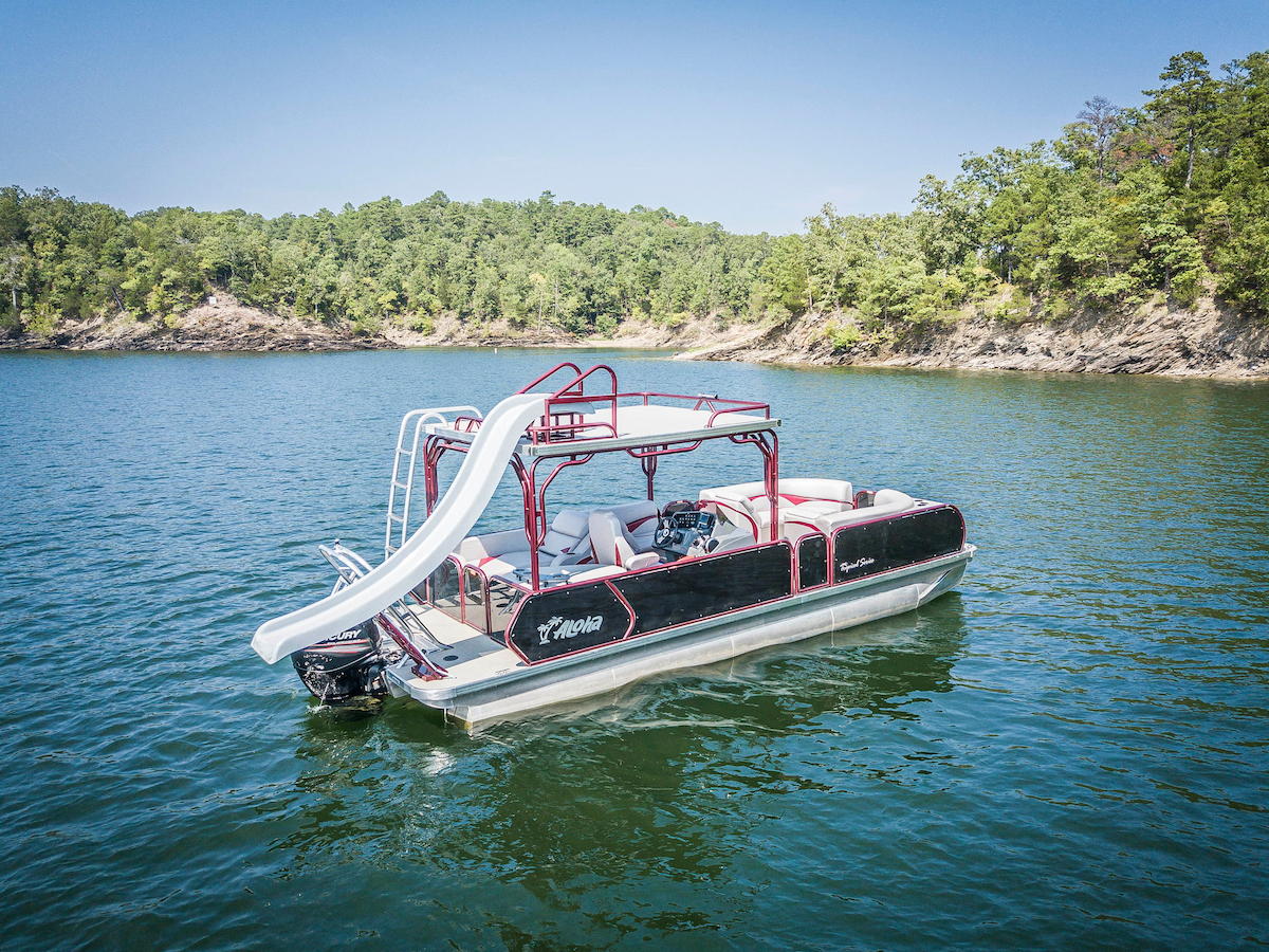 Pontoon boat with a slide on a lake under a clear blue sky.
