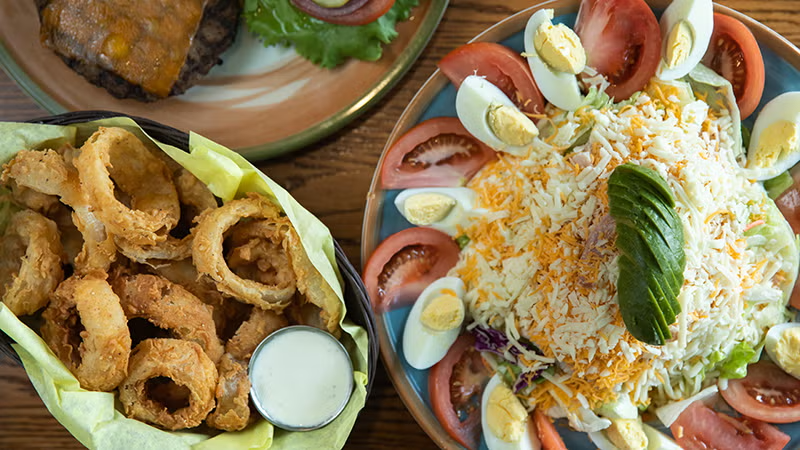 Onion rings, burger, and a salad with eggs and tomatoes.