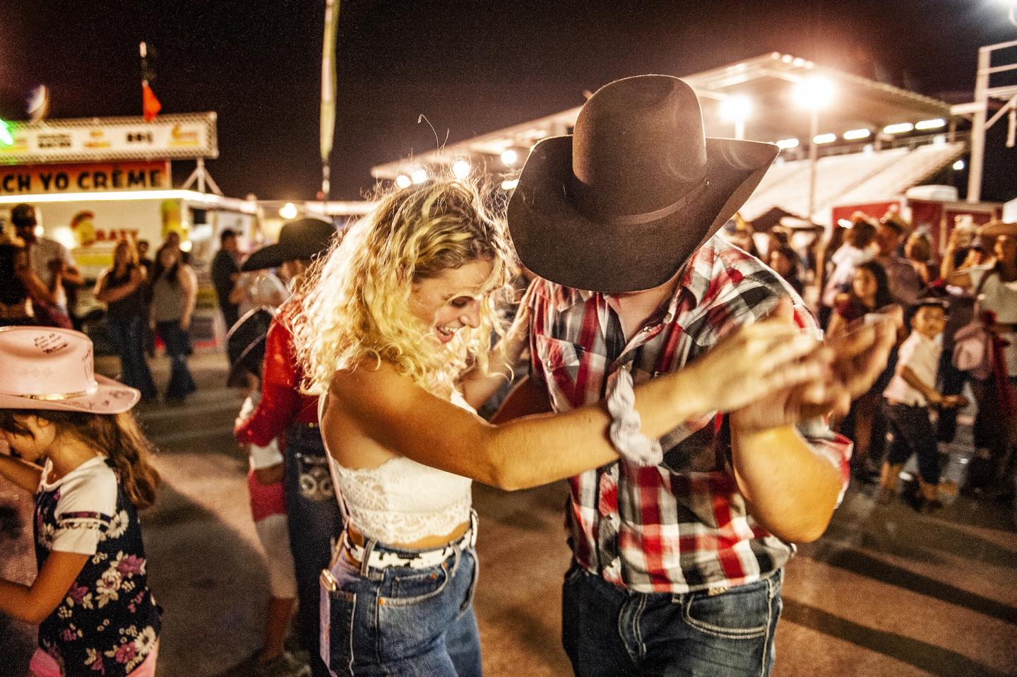 Cowboy-hatted couple dancing outdoors at night, lively crowd in background.