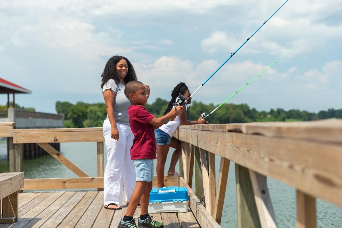Family fishing on a pier, two kids holding fishing rods, sunny day.