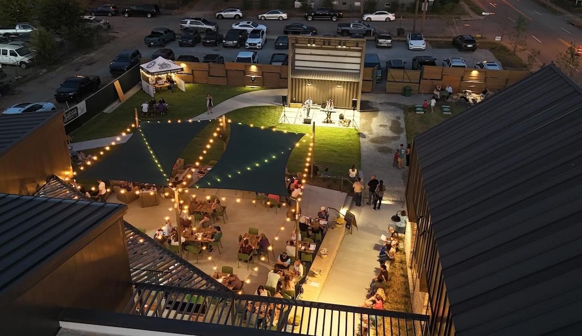 Night rooftop gathering with string lights and people mingling.