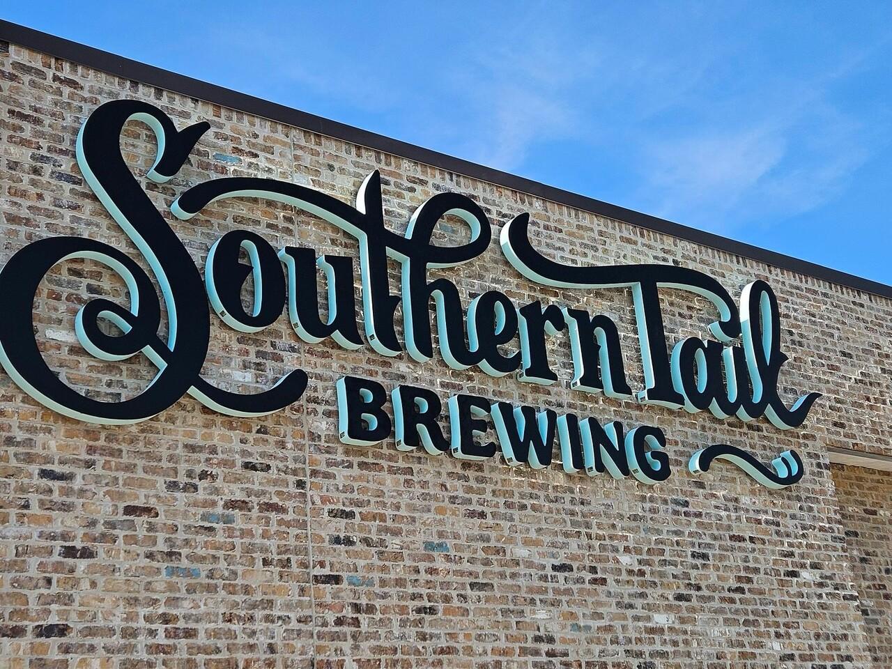 Southern Tail Brewing logo on a brick wall under a blue sky.