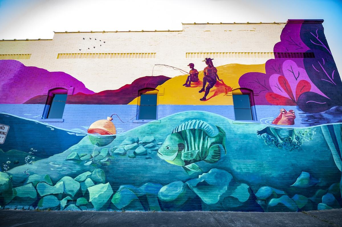 Colorful mural depicting underwater and fishing scenes on a building wall.