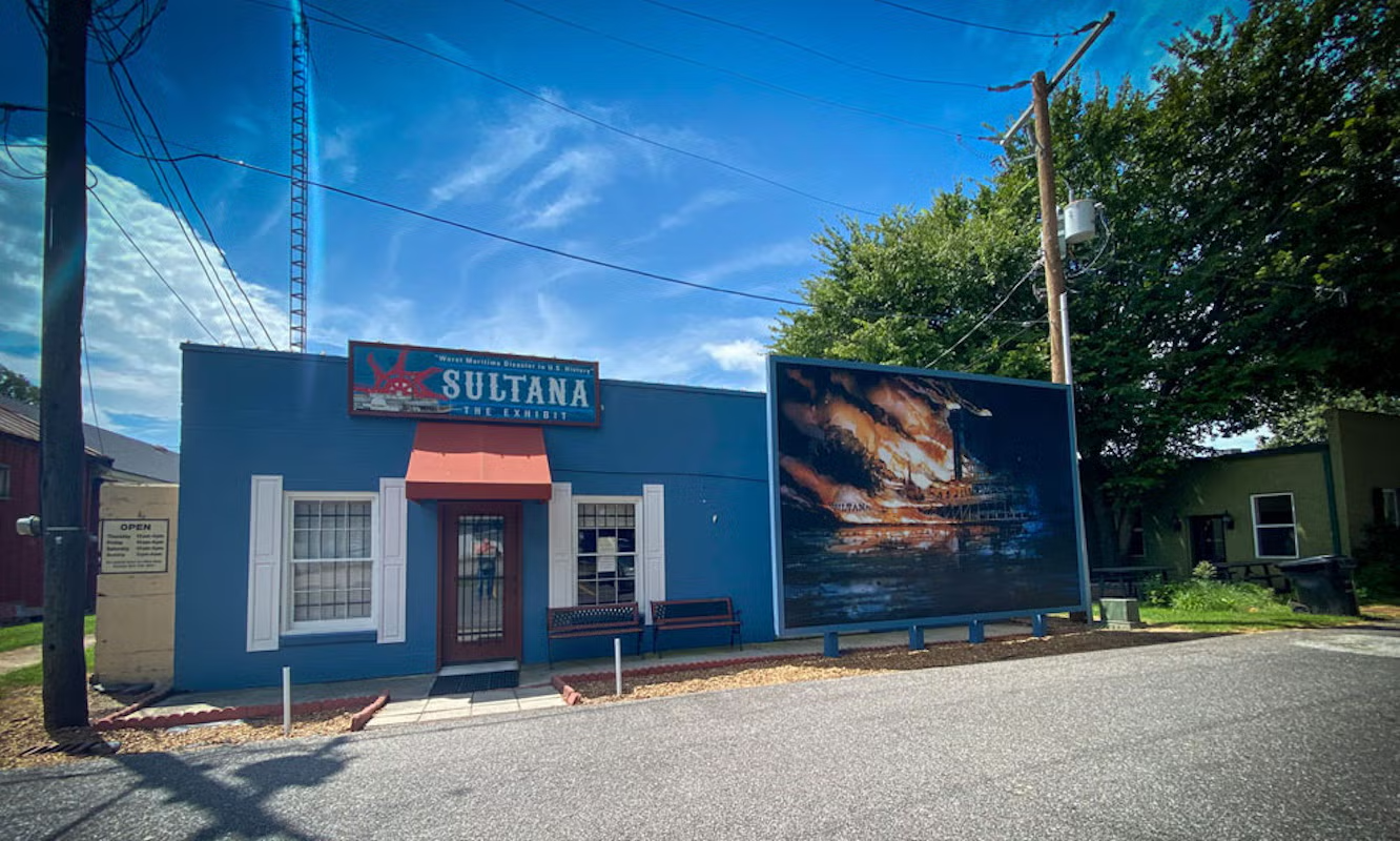 Blue building with a mural, sunny day, tree on the right.