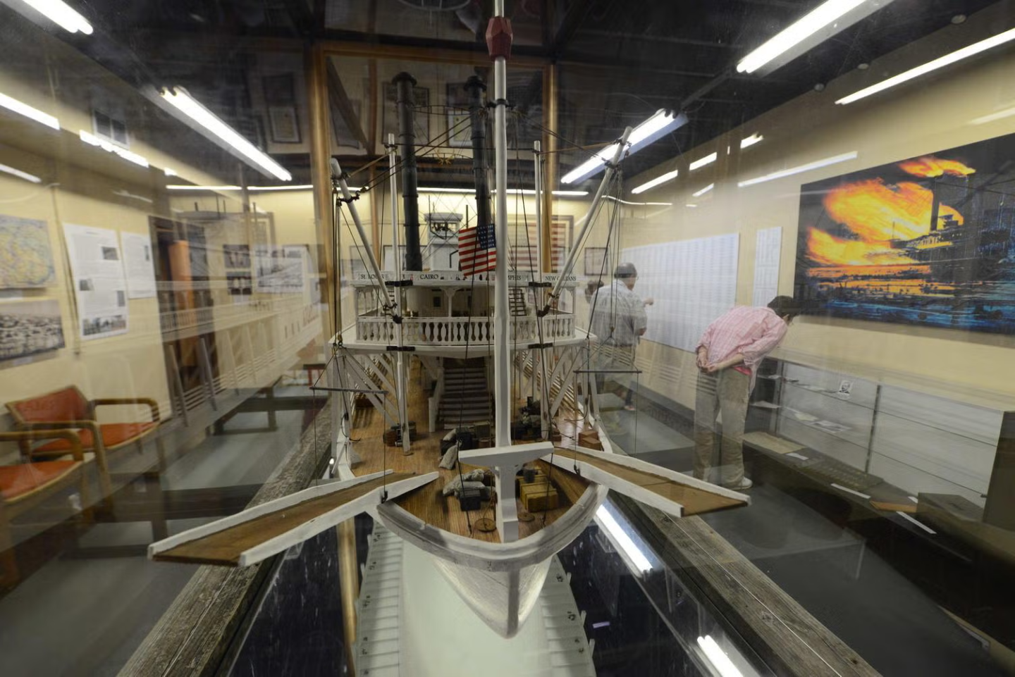 Model ship in museum display, with two people observing nearby.