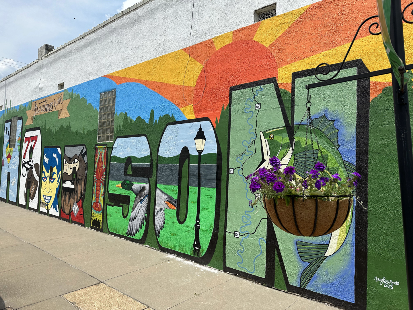 Colorful mural on a wall with a sun, landscape, and flowers.