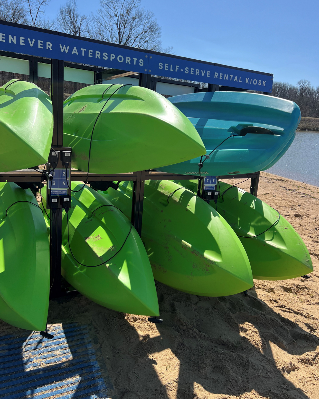 Green and blue kayaks stacked on a sandy beach under a clear blue sky.