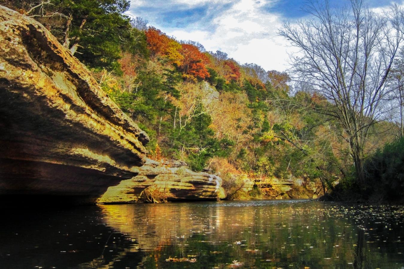 Rocky cliff by a calm river, autumn trees reflected in water.