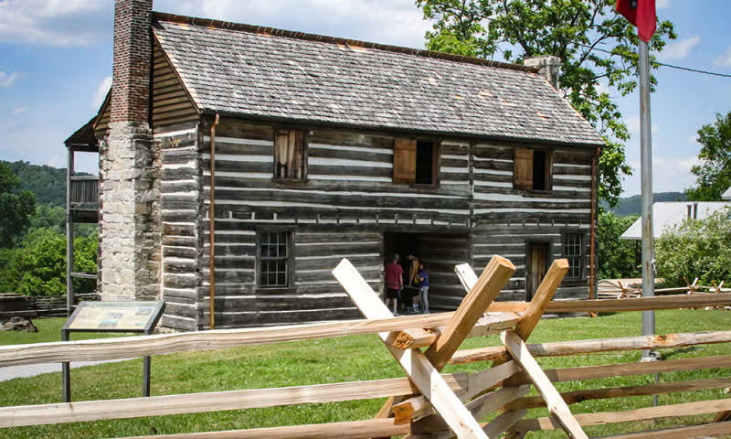 Historic log cabin with a wooden fence and green lawn.