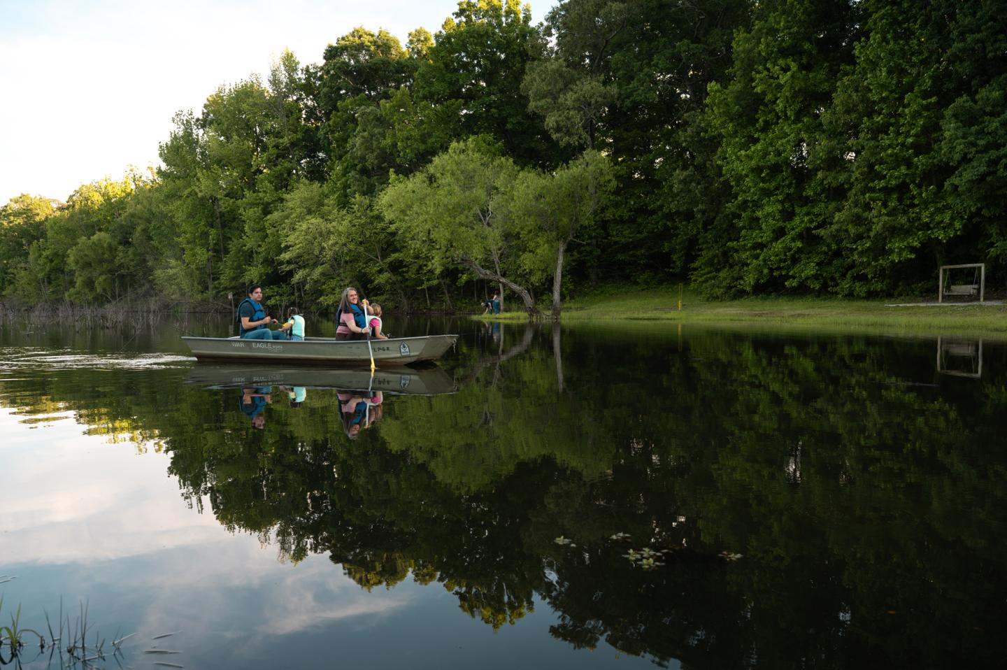 Boat with two people on a calm, tree-lined lake.