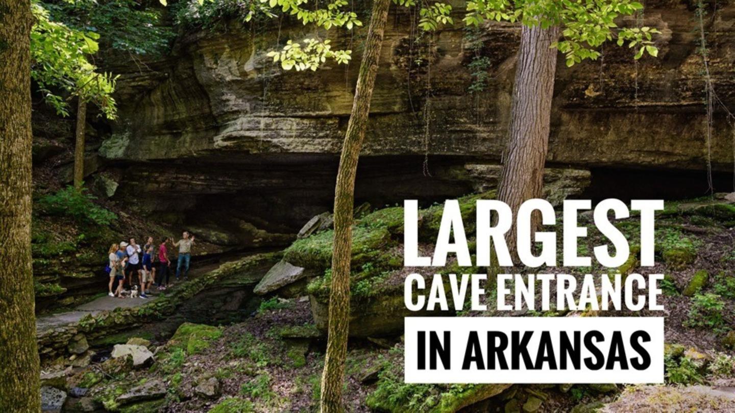 Cave entrance in a forest with visitors nearby.