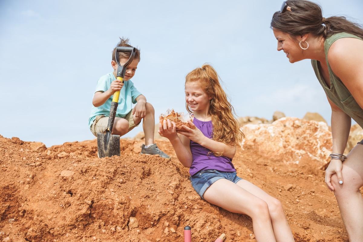 Children and a woman examining rocks on a dirt hill.