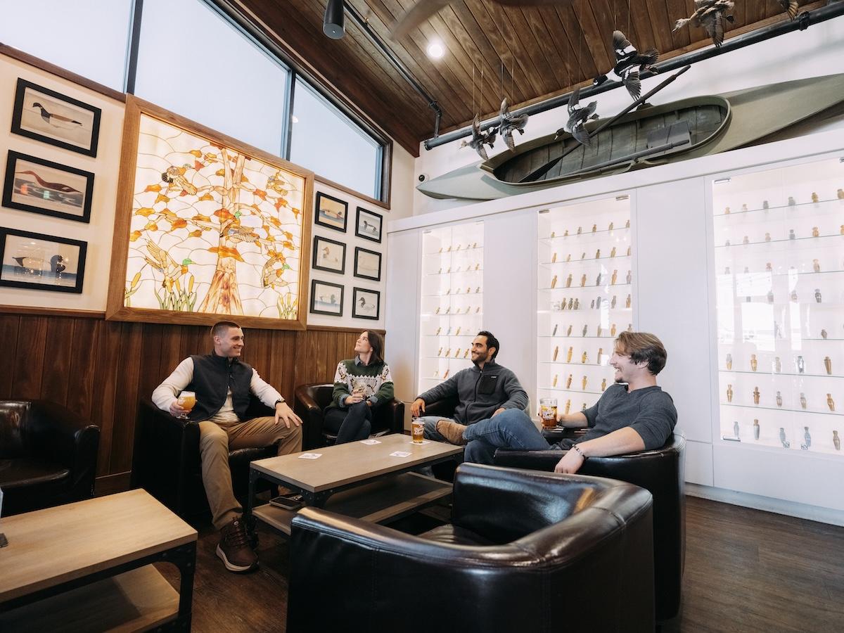 Cozy meeting room with four people chatting in leather chairs under a boat decor.