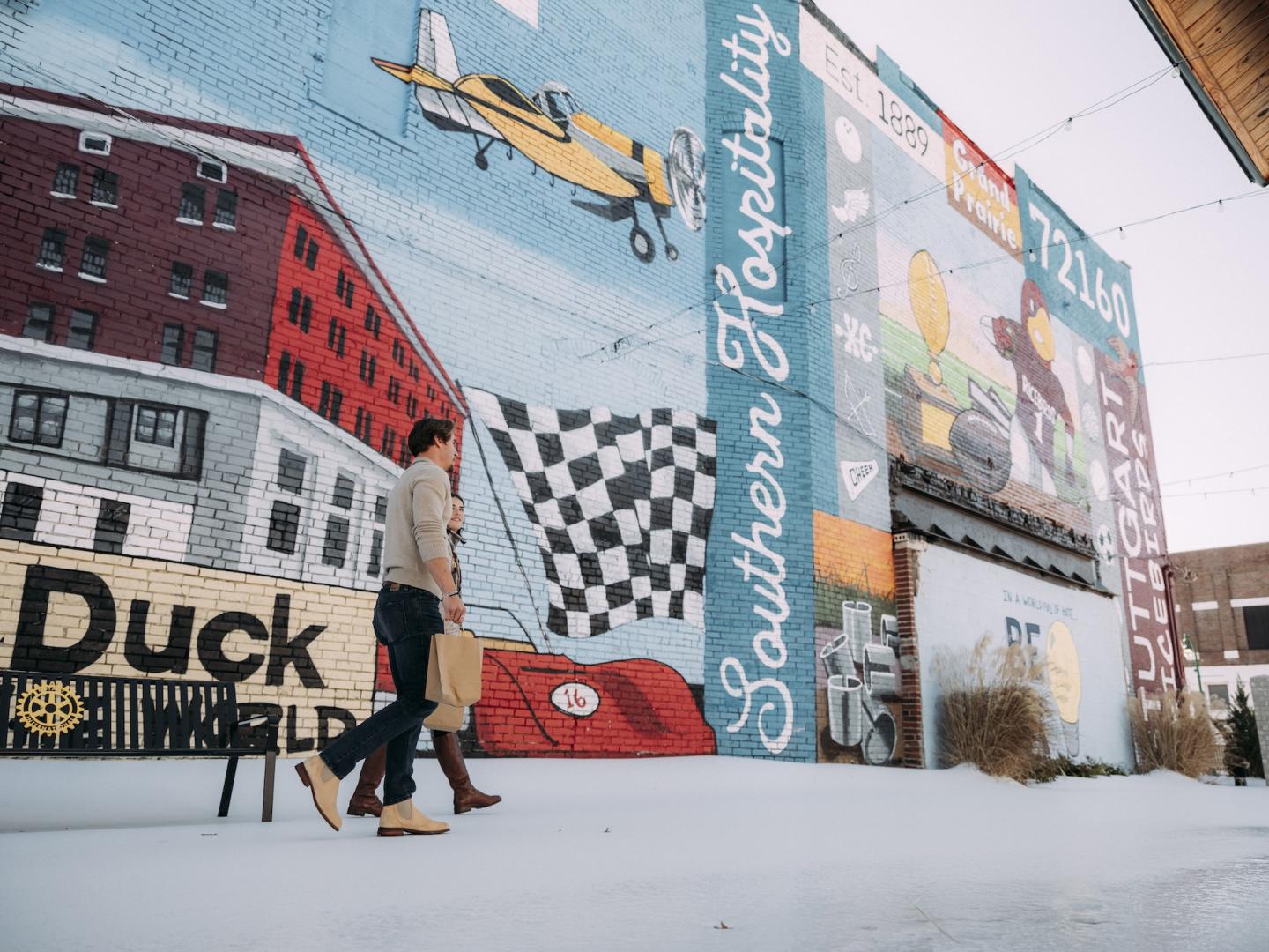 Mural with vibrant colors and text on a brick wall, people walking past.