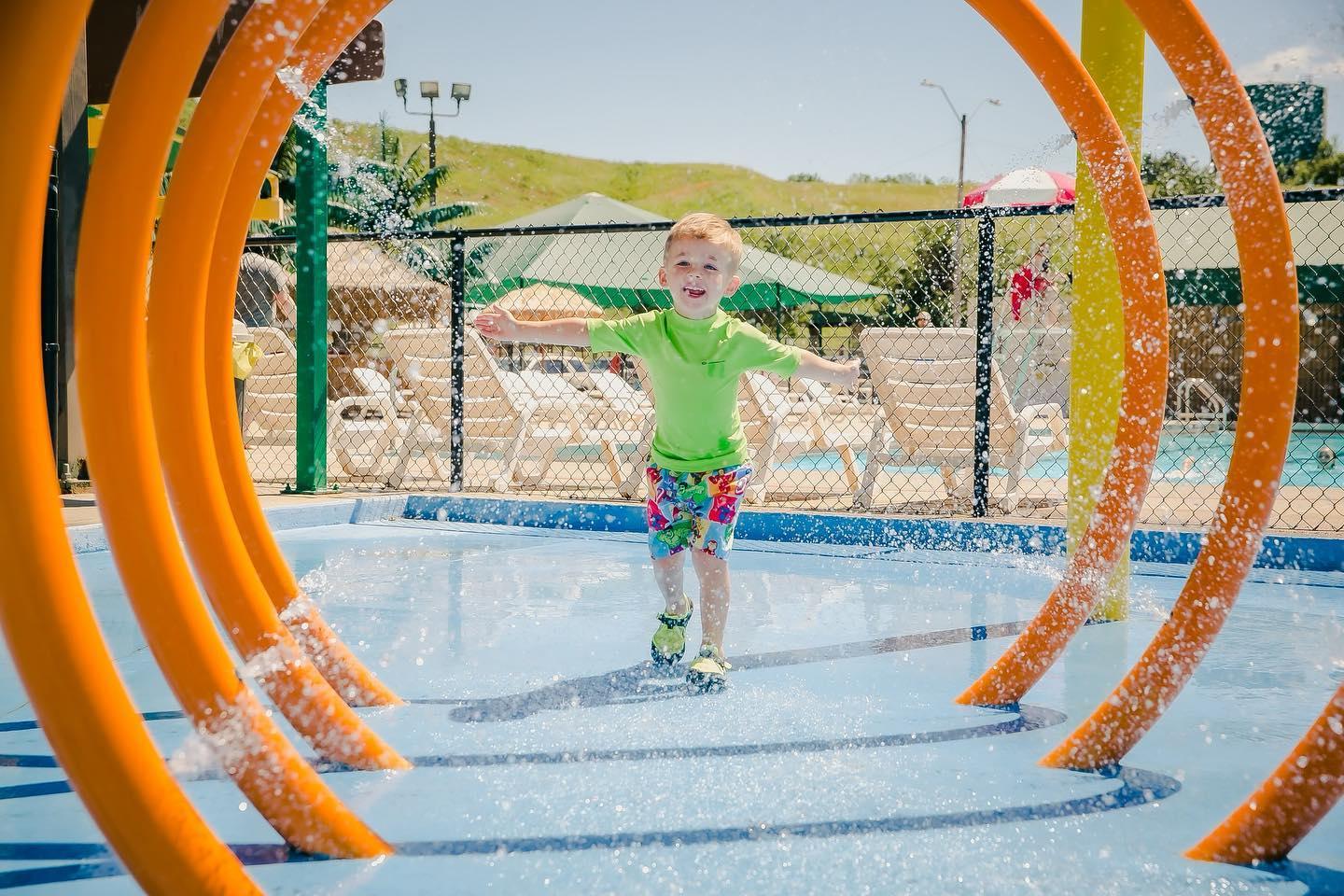 Child playing in water park, running through orange hoops, smiling on a sunny day.