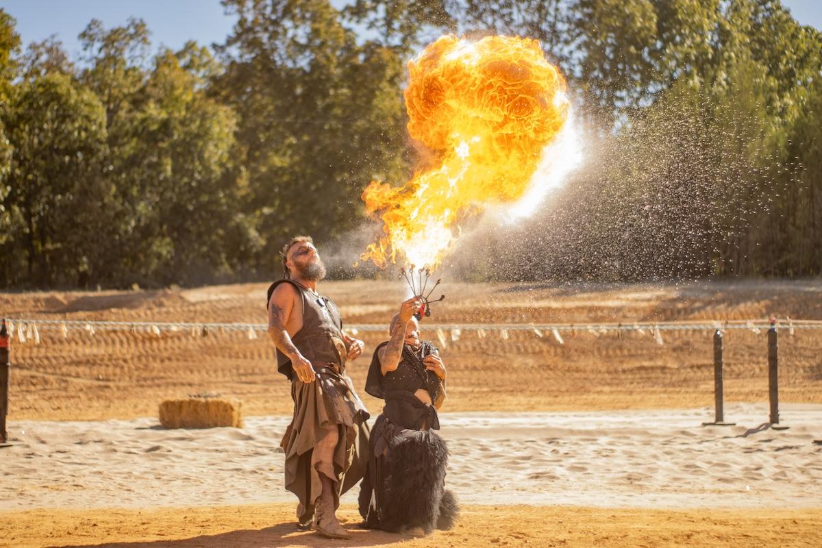 Fire performer blowing flames outdoors during the day.