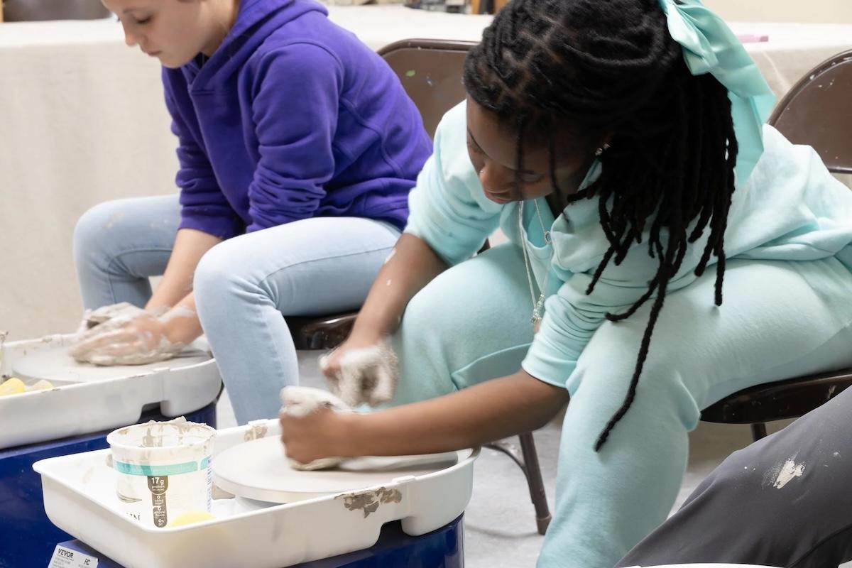 Two people focused on shaping clay on pottery wheels.