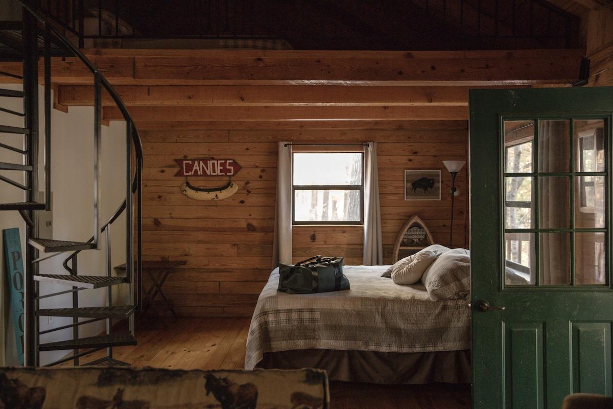 Rustic cabin bedroom with spiral staircase, wooden walls, and a bed by a window.