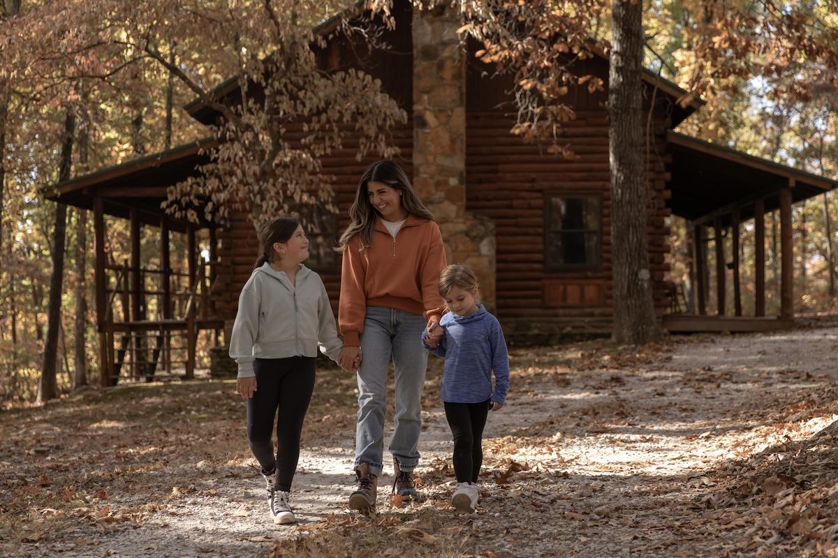 Family walking on a forest path in autumn near a wooden cabin.