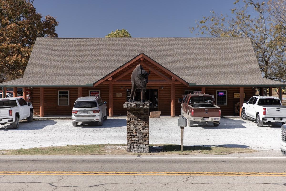 Log cabin-style building with parked trucks and a bull statue in front.