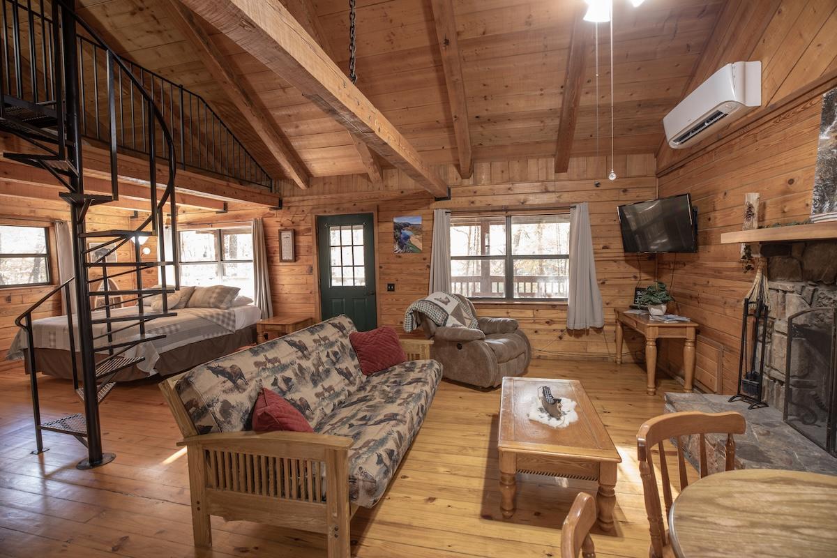 Cozy wooden cabin interior with sofa, spiral staircase, and fireplace.