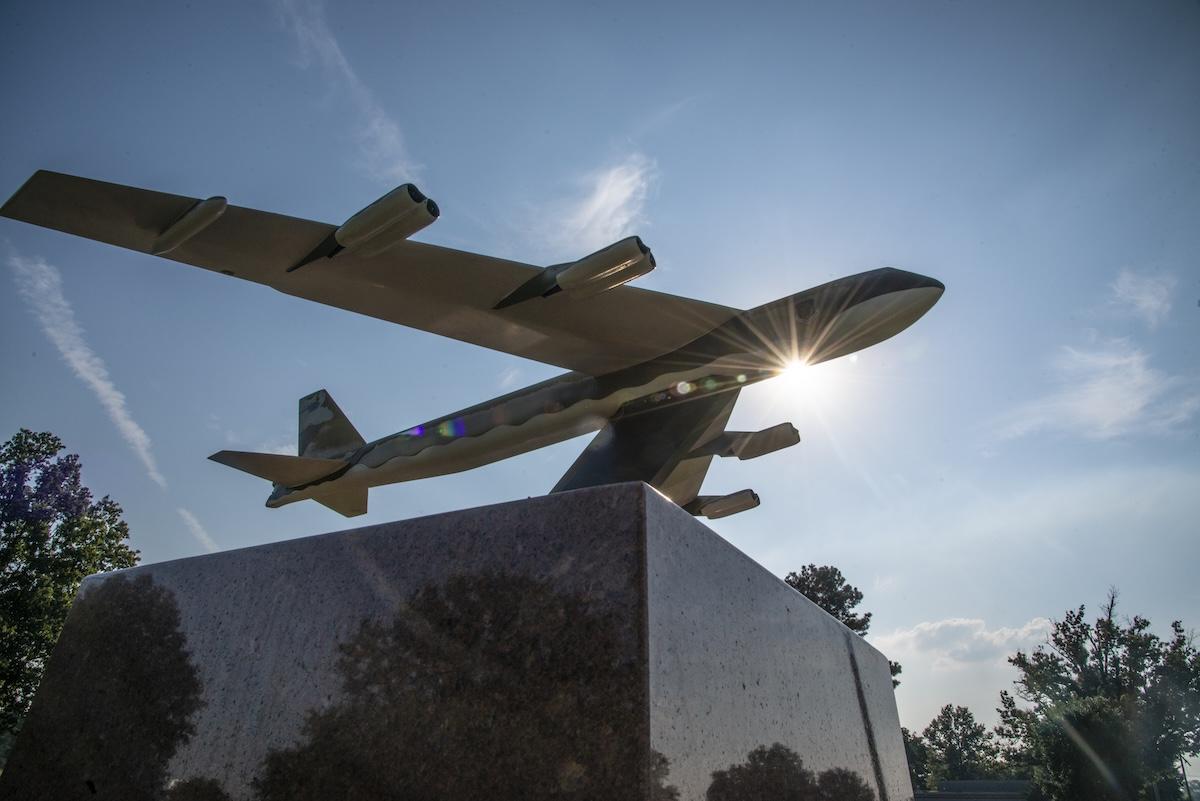 Model airplane sculpture on pedestal with sun behind.