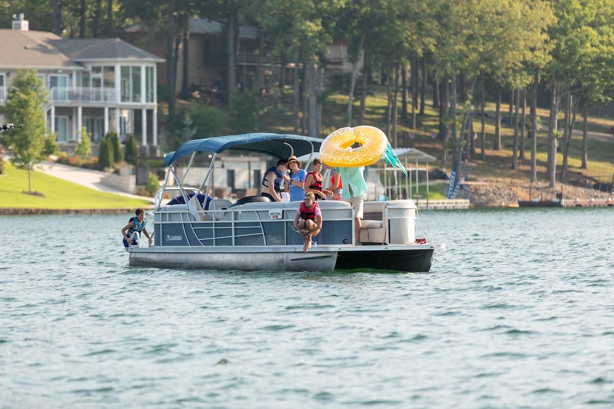 Pontoon boat on a lake with people and a large inflatable tube.
